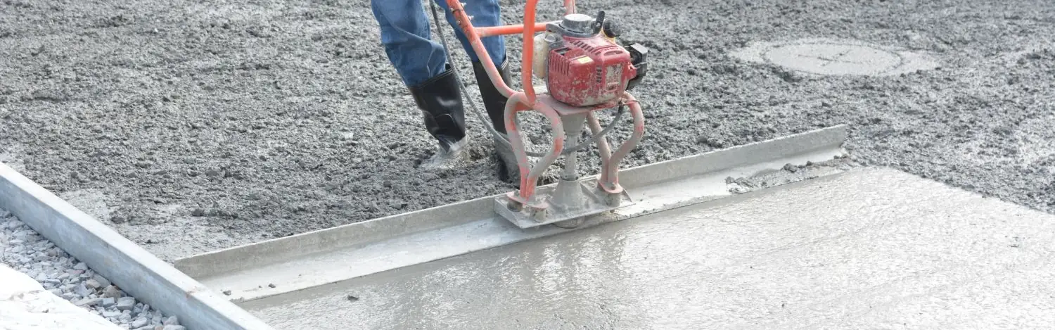 Concrete crew screeding a fresh slab level between the forms