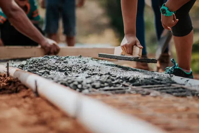Concrete finisher pulling a screed board across wet concrete