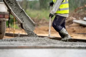 Professional concrete contractors in Fort Worth TX carefully spreading fresh concrete, worker wearing safety gear and high-visibility vest ensuring proper concrete distribution